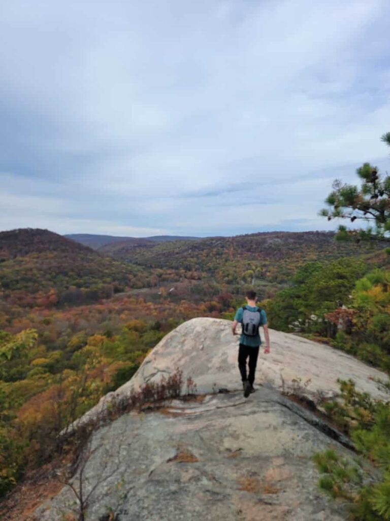 A young man walks down a path over a large boulder
