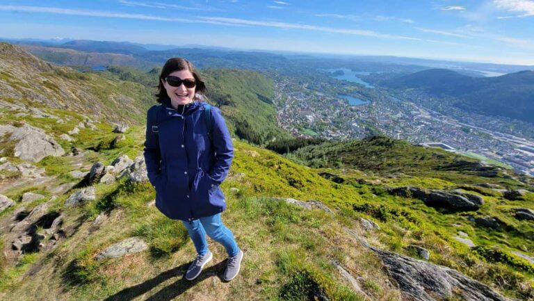 A woman stands on a cliff with an expansive view in the distance
