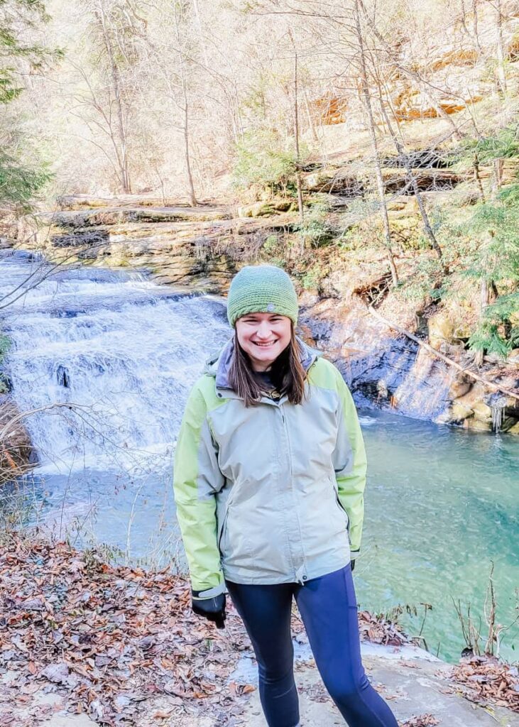 A woman stands on a ridge in front of a waterfall
