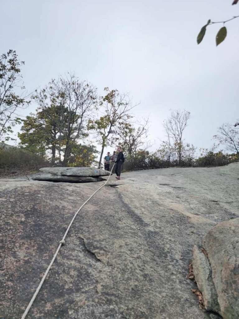 A young girl descend a flat rock using a rope to assist