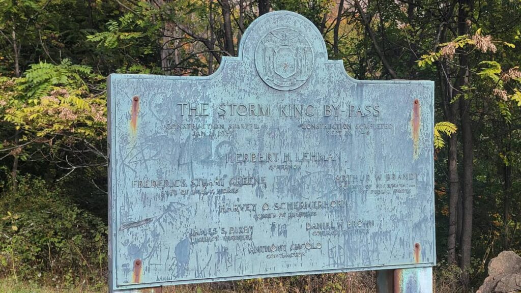 A metal historical marker sign reads "Storm King By Pass"