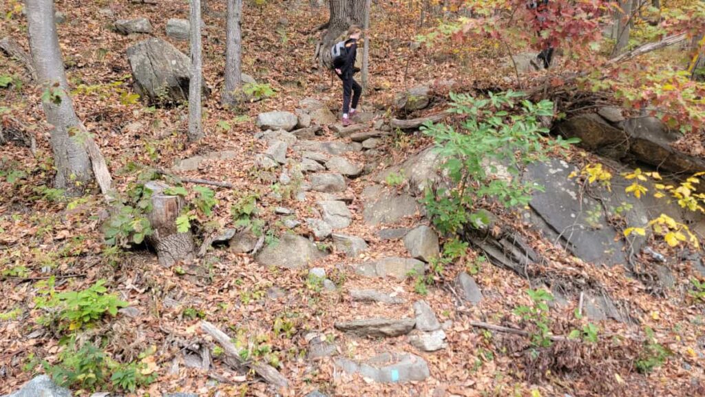 A girl hikes up stone steps at the start of the Popolopen Trail