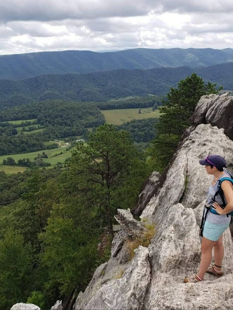 A woman stands on rock outcroppings looking over a valley