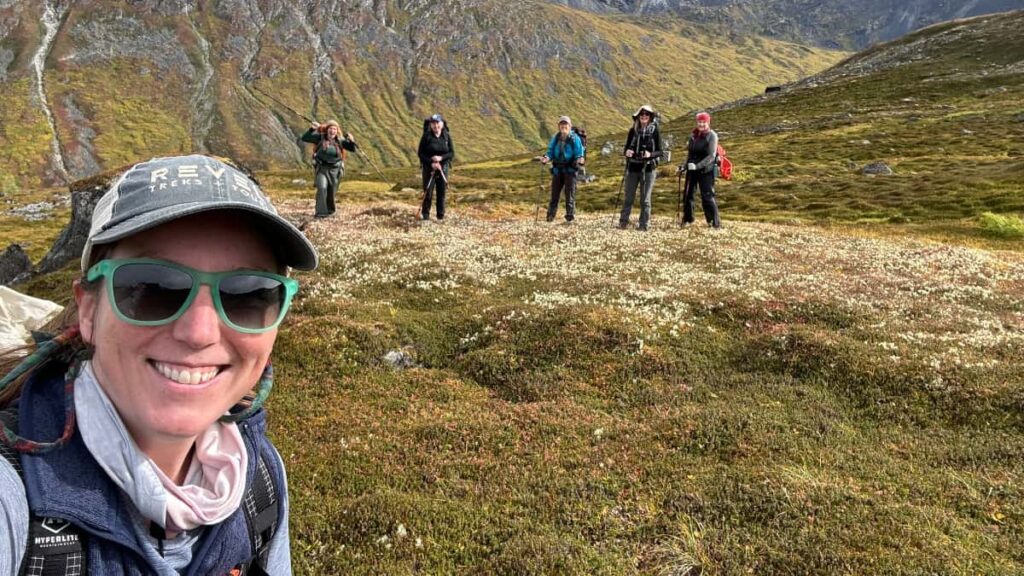A woman takes a self portrait with hikers standing in a line a distance behind her