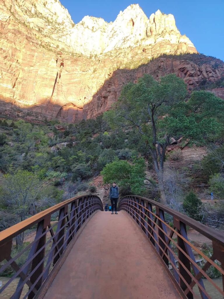A teen boy stands on the footbridge leading to the Emerald Pools Trail