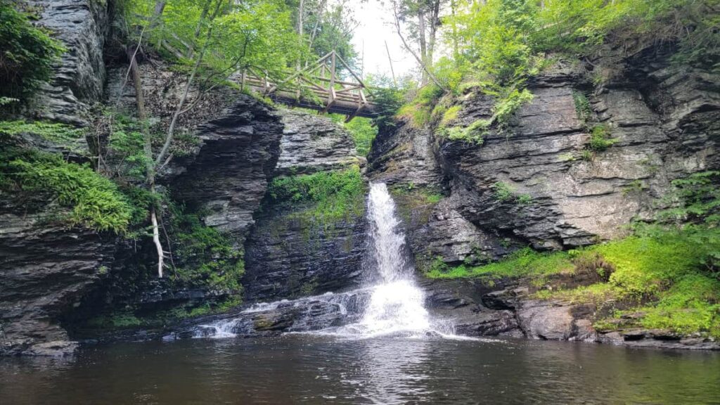 A skinny waterfall flows under a footbrigde