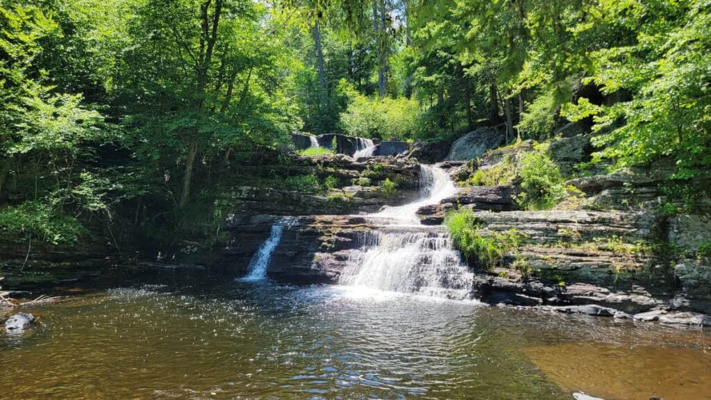 A multi level waterfall flows into a shallow pool