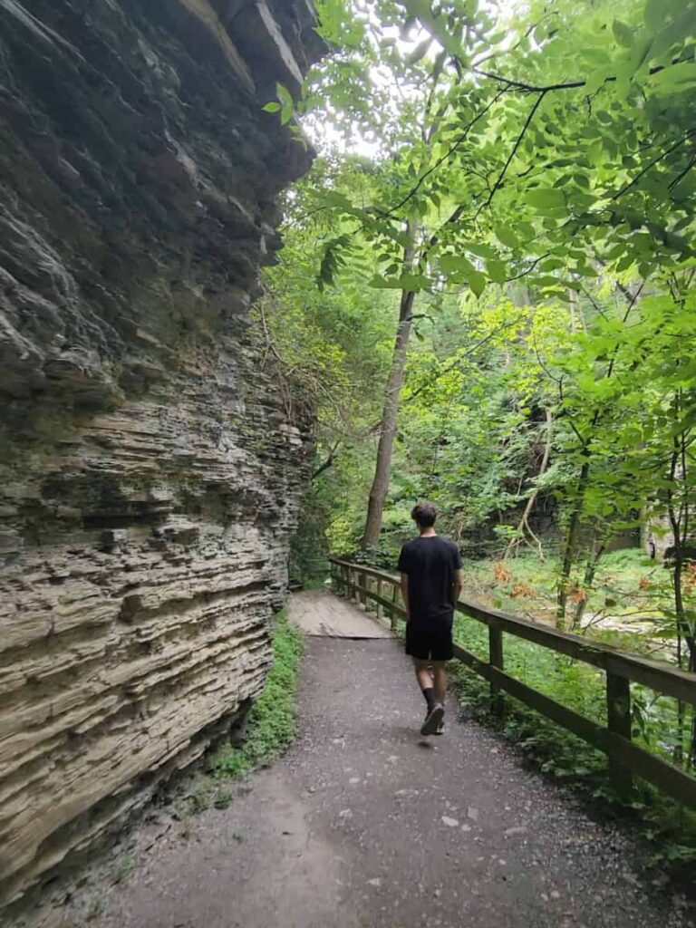 A teen walks along a flat dirt path to Eagle Cliff Falls