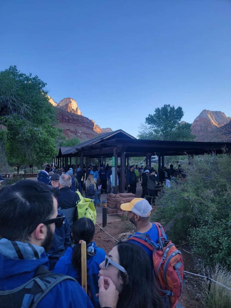 Visitors stand in a long line waiting to get on the shuttle at Zion National Park